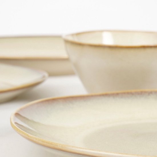 Stapel beige stenen borden en kommen met een bruine, verweerde rand.