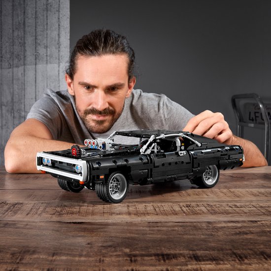 Een man bouwt aan een zwarte LEGO Technic Dodge Charger met een dikke motor.