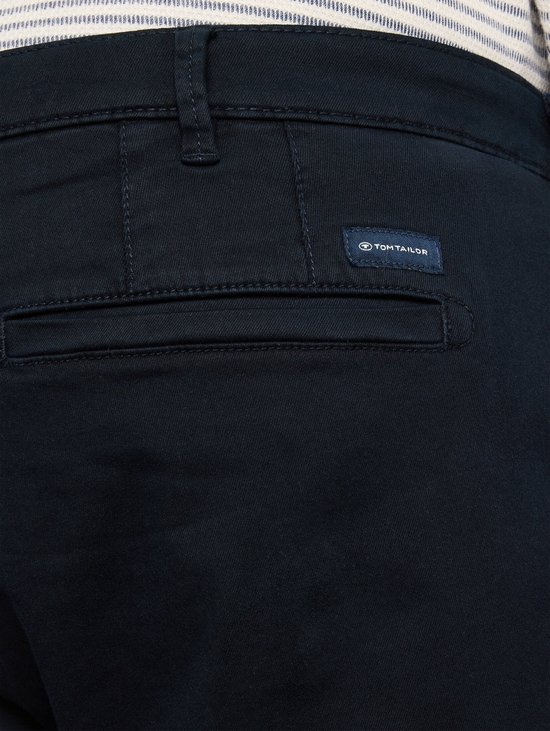 Detail van een marineblauwe chino met paspelzak en een blauw 'TOM TAILOR' label.