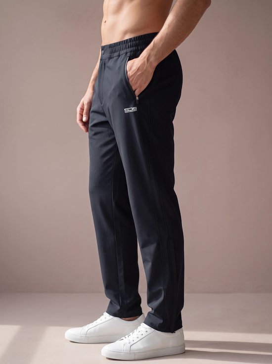 Zijzicht van een man die een donkerblauwe sportbroek draagt, met logo op de zijkant en witte sneakers.
