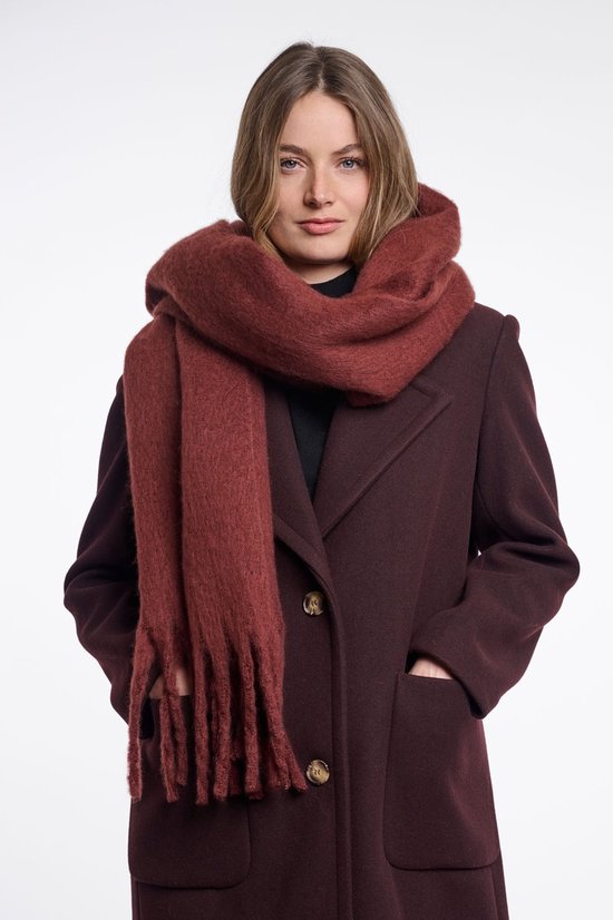Vrouw met een oversized, donkerrode sjaal met franjes om haar nek. Ze draagt een bordeauxrode jas.