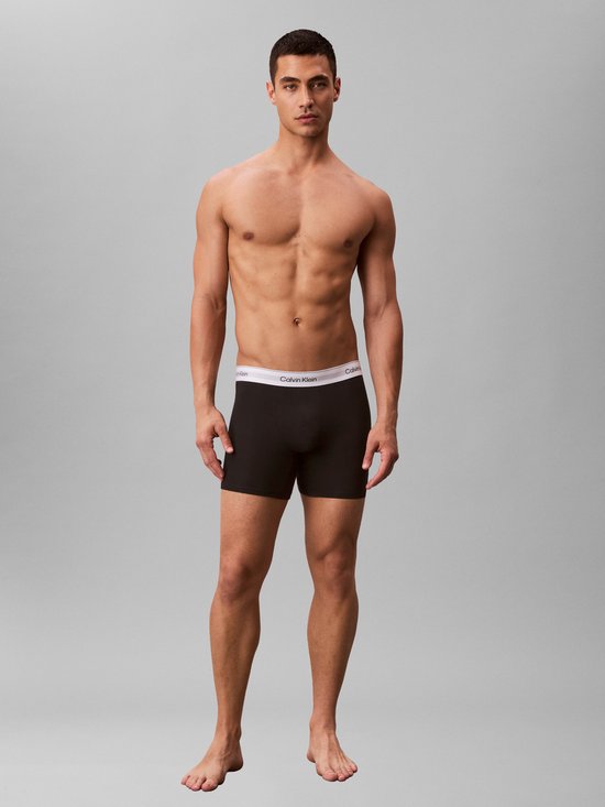 Man, staand, in zwarte Calvin Klein boxershorts met witte logo tailleband.
