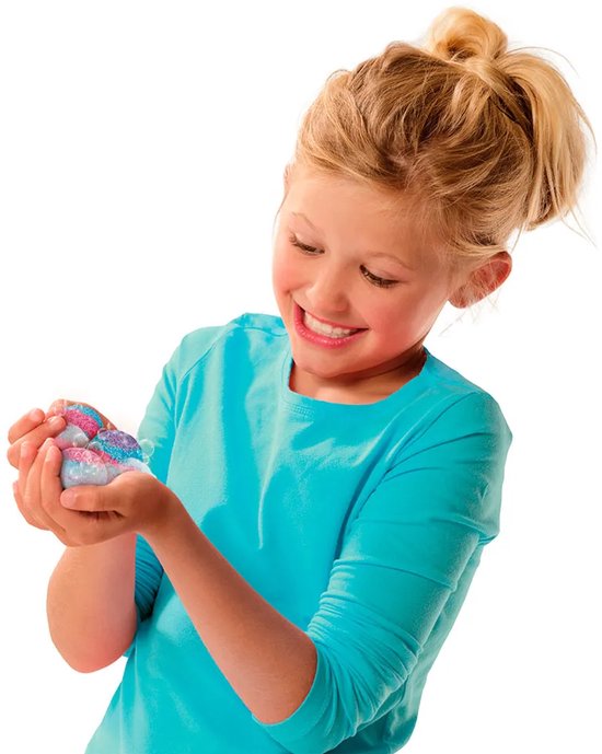 Een lachend meisje met een blauw shirt houdt kleine, roze en blauwe badbruisballetjes vast in haar handen.