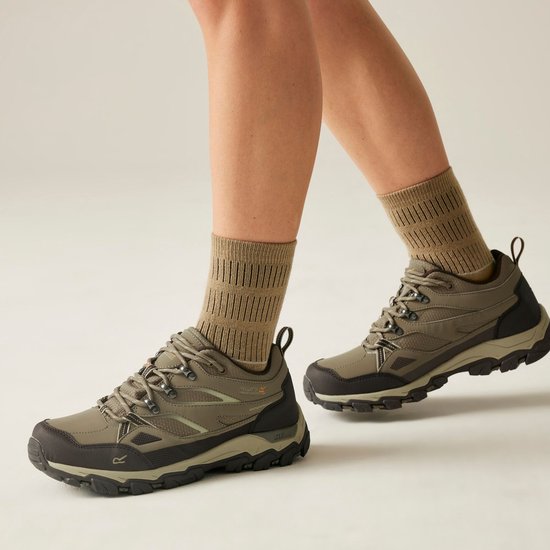 Model draagt bruine wandelschoenen met beige sokken, wandelend in een lichte studio-omgeving.