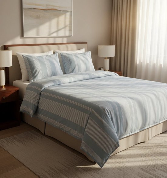 Blauw gestreept dekbedovertrek op een bed met beige hoofdbord, twee lampen en een raam met gordijnen.