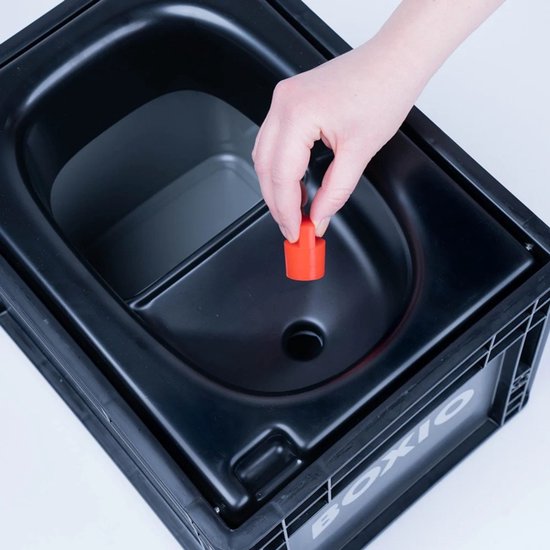 Hand voegt een oranje dop toe aan het zwarte toilet, met BOXIO logo op de zijkant.