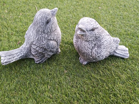Twee betonnen vogels, een met grijs geschubd verenpatroon, liggend op gras.