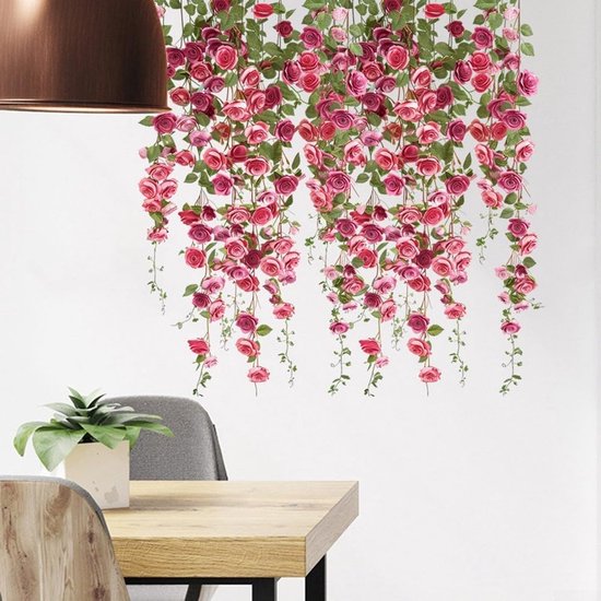 Hangende roze en rode rozen met groene bladeren tegen een witte muur.