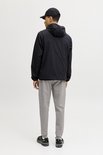 Man van achteren gezien met zwarte jas, grijze joggingbroek en zwarte sneakers. Witte achtergrond.