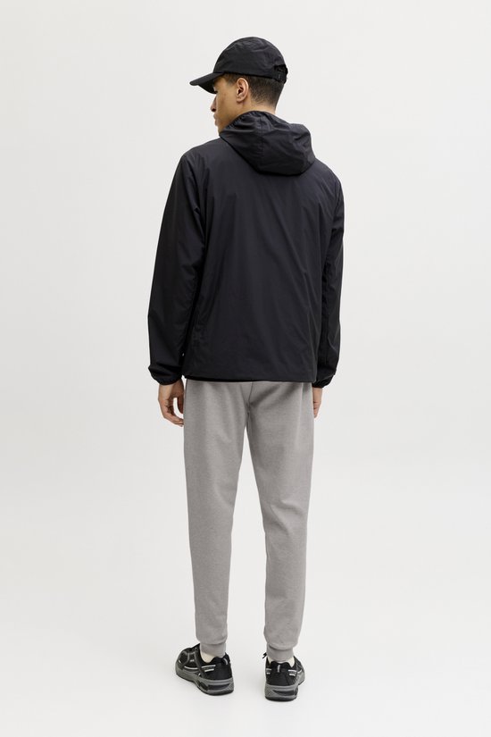 Man van achteren gezien met zwarte jas, grijze joggingbroek en zwarte sneakers. Witte achtergrond.