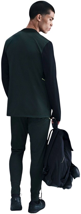 Man in donkergroen en zwart Nike trainingspak, van achteren gezien.