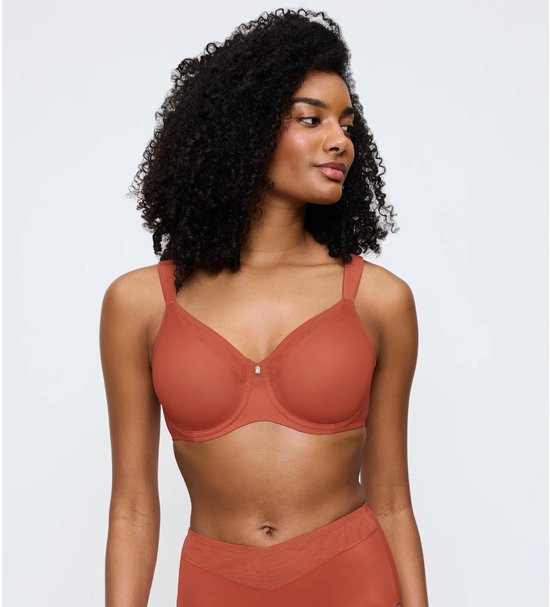 Model draagt een koraalkleurige beha met beugels en verstelbare bandjes. De beha heeft een klein detail bij de cups.