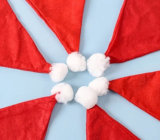 Rode kerstmutsen met witte pompons, gerangschikt in een cirkel op een blauwe achtergrond.
