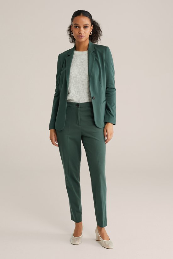 Model draagt een donkergroene blazer en bijpassende broek met een gebreide top.