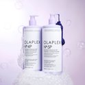 Twee lichtpaarse flessen, één met pompdispenser en één met schroefdop, op een witte achtergrond met bubbels.