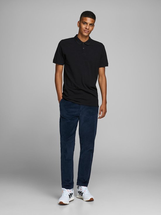 Zwarte polo met korte mouwen, gedragen door een man in een corduroy broek en sneakers. Volledige outfit.