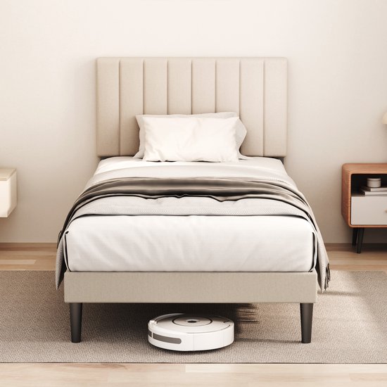 Eenpersoonsbed met gestoffeerd, verticaal gestreept hoofdbord in beige stof. Een wit kussen en een grijze deken liggen op het bed.