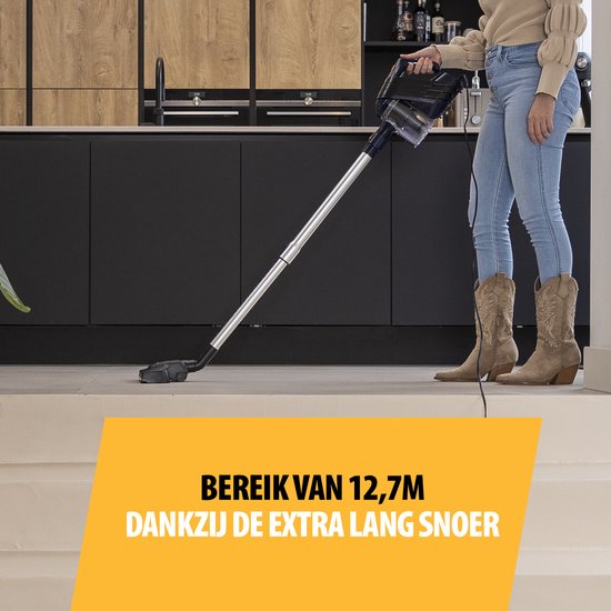 Vrouw in spijkerbroek en cowboylaarzen met blauwe steelstofzuiger in een keuken. Tekst: Bereik van 12,7m.
