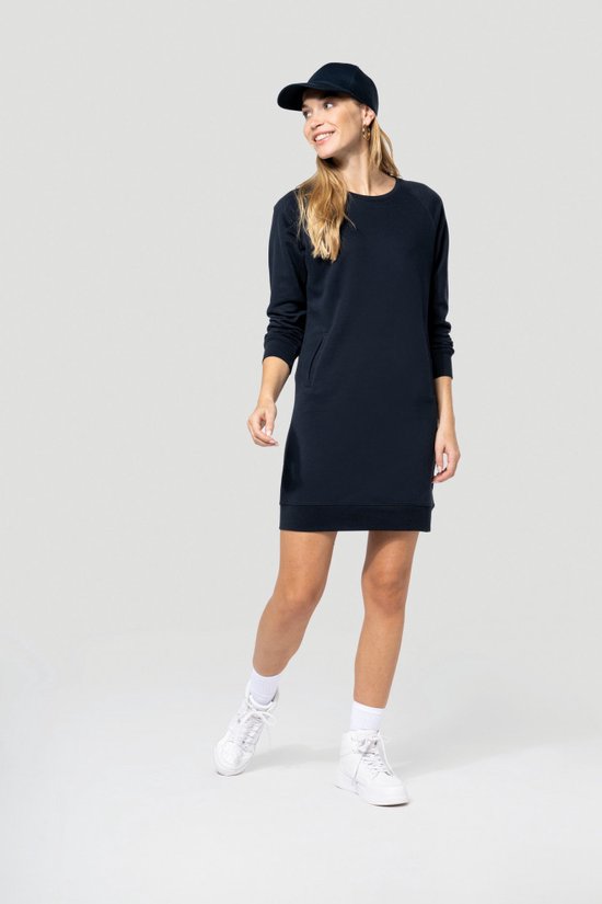 Model draagt een donkerblauwe jurk, pet, witte sokken en sneakers.