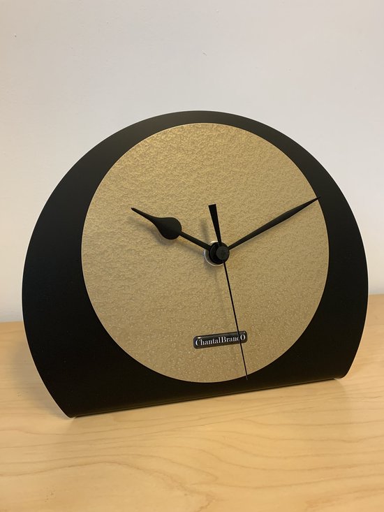 Horloge de table noir, semi-circulaire, avec un cadran doré et des aiguilles noires. Logo ChantalBrando en bas.