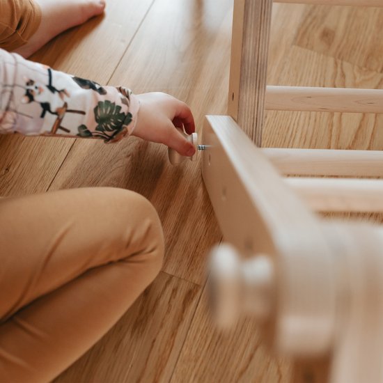 Kind handen draaien aan een schroef in een houten klimrek.