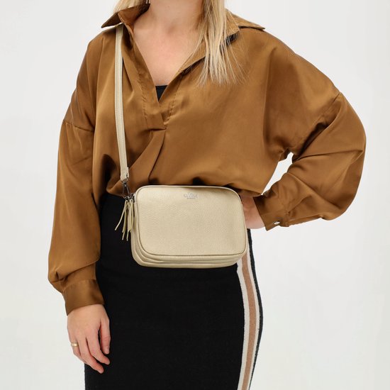 Model met gouden crossbodytas van Charm London, gedragen over een bruine blouse en zwarte rok.