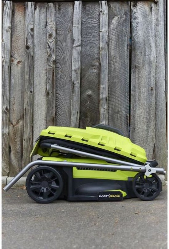 Groene en zwarte Ryobi grasmaaier ingeklapt, staand tegen een houten schutting.