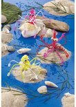Geknutselde spinnen en octopussen van glinsterende, veelkleurige Filofun-draden, zittend op schelpen en zand.