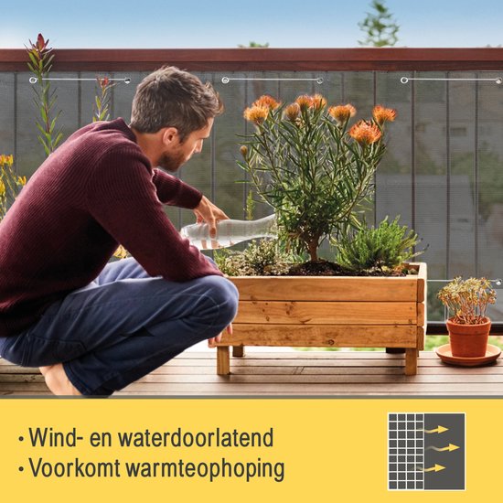 Man die planten water geeft op een balkon met donkergrijs balkondoek. "Wind- en waterdoorlatend. Voorkomt warmteophoping".