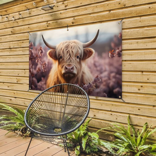 Een bruine Schotse hooglander met lange, golvende vacht staat in een veld met roze bloesems. De poster hangt aan een houten schutting, naast een stoel.