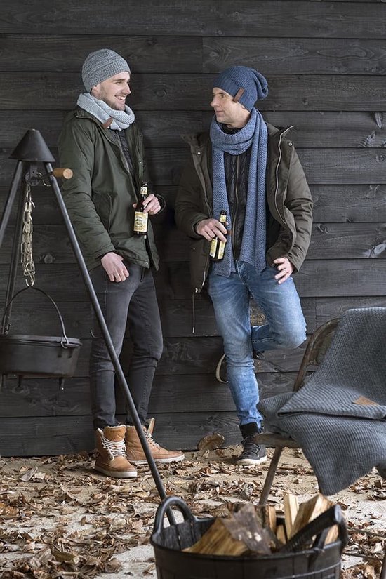 Twee mannen met mutsen en sjaals, staand tegen een houten muur, met flessen bier in hun handen.