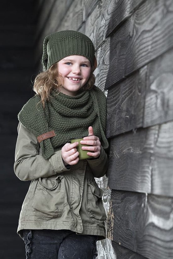 Een jong meisje met golvend haar, draagt een mosgroene gebreide muts en sjaal, met een kaki jasje.