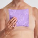 Vrouw houdt paarse, bloemvormige individuele verpakking van TENA Discreet pad vast.