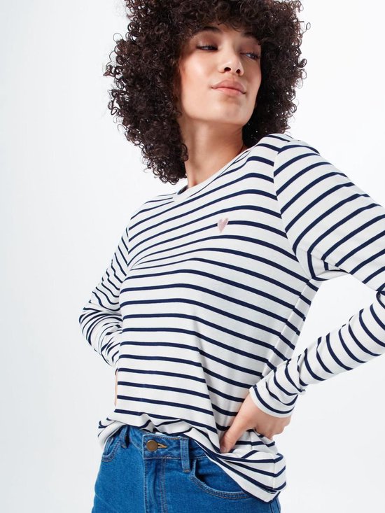 Model met krullend haar draagt een wit T-shirt met lange mouwen, gestreept met marineblauw, en een klein roze hartje op de borst. Spijkerbroek.