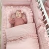 Baby in roze kleding ligt in een roze babynestje met ruches, naast een dekbed.