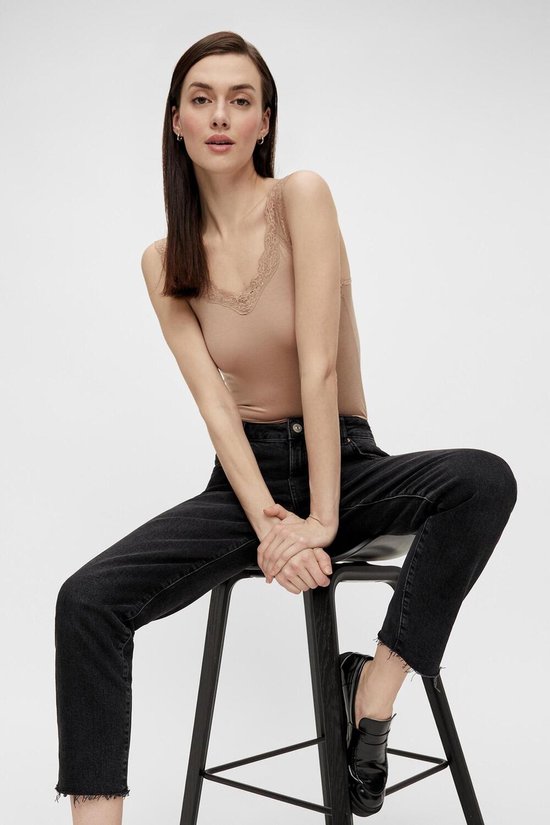 Model in beige hemd met kanten rand, zittend op een krukje met zwarte jeans.