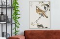 Une estampe japonaise d'un oiseau sur une branche aux fleurs jaunes, suspendue au-dessus d'un canapé brun rouille.