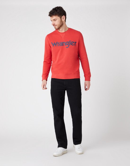 Man in een zwarte jeans en rode Wrangler sweater, staand, voorkant.