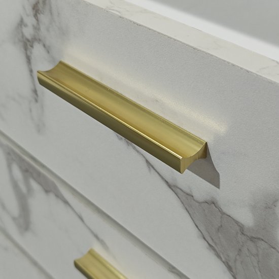 Close-up van een gouden handvat op een wit marmerlook dressoir.