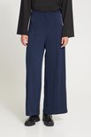 Model draagt een donkerblauwe broek met wijde pijpen, diagonaal patroon en zwarte schoenen.