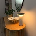 Witte Pilia tafellamp op een houten console tafel naast een plant en een spiegel.