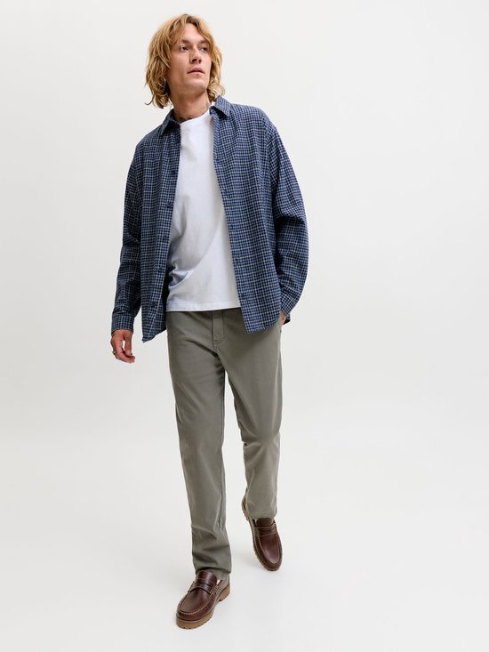 Man met blonde haren, draagt grijze chino, wit T-shirt en blauw geruit overhemd.