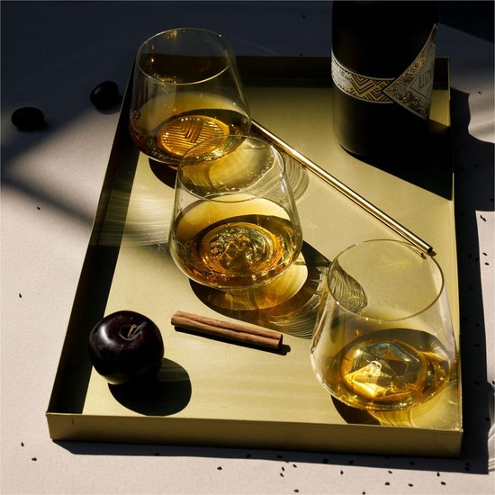 Verres tulipes dorés avec une boisson ambrée, sur un plateau doré avec prune et cannelle.
