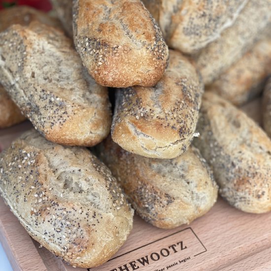 Stapel kleine broodjes met sesamzaad en maanzaad op een houten plank.