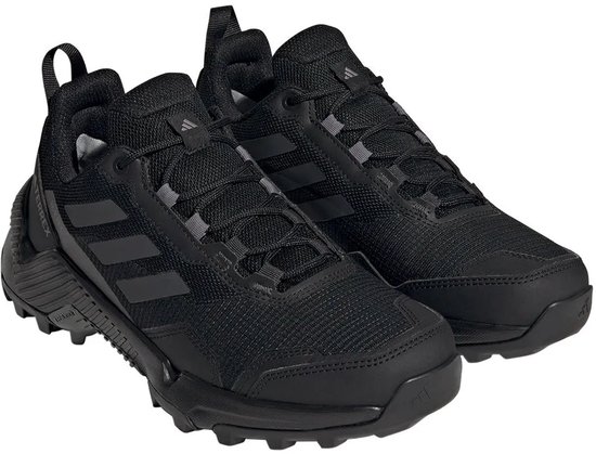 Een paar zwarte dames wandelschoenen met zwarte Adidas-strepen, veters en een robuuste zool.