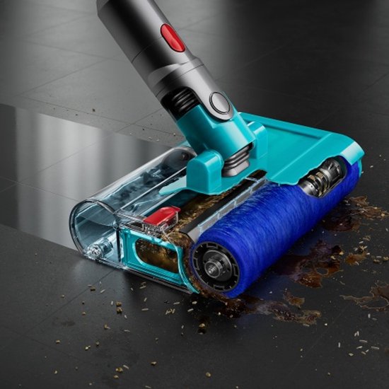 De mond van de stofzuiger met een turquoise behuizing en een blauwe borstel verwijdert kruimels en vlekken van een donkere tegelvloer.