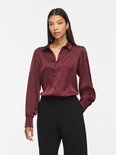 Model draagt bordeauxrode satijnen blouse met lange pofmouwen, kraag en knoopsluiting.