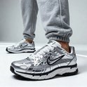 Een persoon draagt grijze Nike P-6000 sneakers met een zilverkleurige metallic finish, gecombineerd met een grijze joggingbroek.
