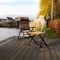 Bruine, verstelbare campingstoel en voetenbankje met donker metalen frame, op een houten terras aan het water.