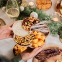 Drie handen houden een borrelplank vast met kaassoorten, worstjes, crackers, noten en dip.
